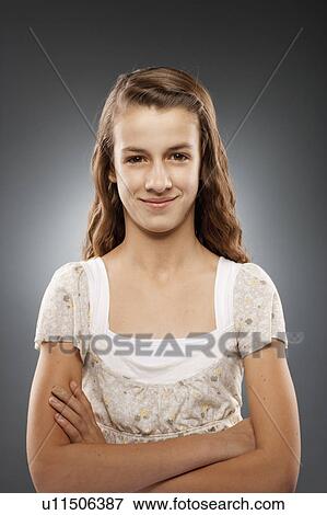 Stock Photo - Portrait of girl (12-13) looking at camera with arms crossed, studio shot. Fotosearch