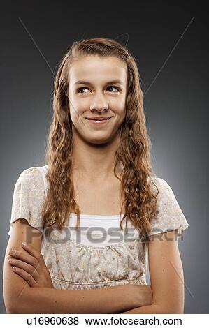 Stock Photo - Portrait of girl (12-13) looking at camera with arms crossed, studio shot. Fotosearch