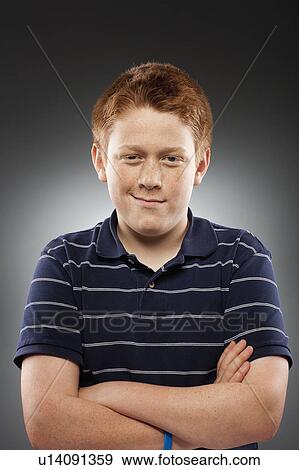 Stock Photo - Portrait of redhead teenage boy (14-15) with arms crossed, studio shot. Fotosearch