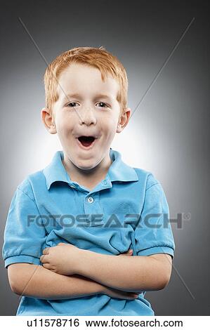 Stock Photograph - Portrait of smiling redhead boy (4-5) wearing blue polo shirt and making face, studio shot. Fotosearch
