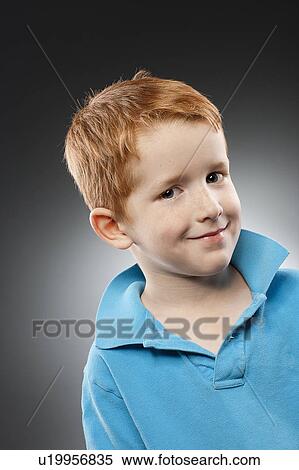Stock Photography - Portrait of smiling redhead boy (4-5) wearing blue polo shirt, studio shot. Fotosearch