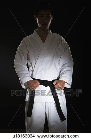Picture - Portrait of young man performing karate stance on black background. Fotosearch