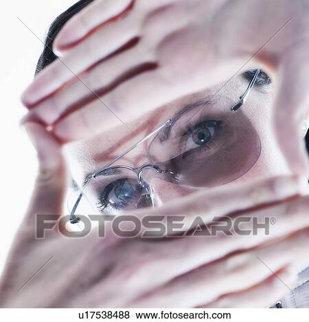 Stock Photo - Portrait of young woman making finger frame over glasses. Fotosearch