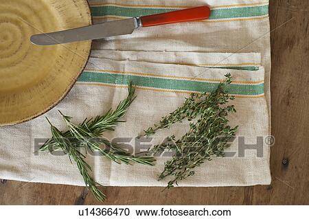 Stock Image - Rosemary and thyme with kitchen knife lying on kitchen cloth, directly above. Fotosearch