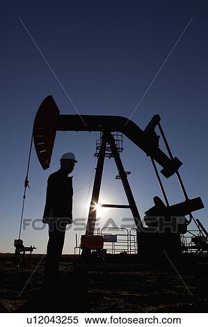 Stock Photography - Silhouette of oil worker by pump jack on rig. Fotosearch