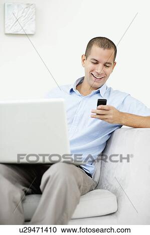 South Africa, Young man sitting on sofa with laptop and texting messages View Large Photo Image Stock Image - South Africa, Young man sitting on sofa with laptop and texting messages. Fotosearch