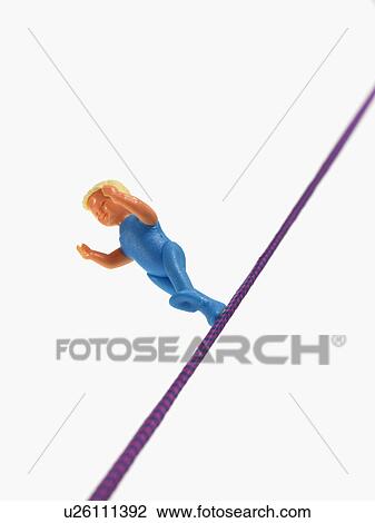 Stock Image - Studio shot of figurine balancing on tightrope. Fotosearch