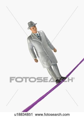 Stock Image - Studio shot of male figurine in suit balancing on tightrope. Fotosearch