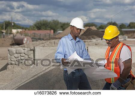 Stock Photograph - Two construction workers discussing blueprints on building site. Fotosearch