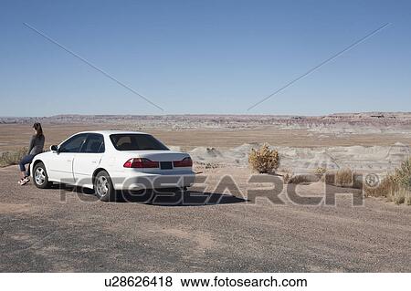 Stock Photo - USA, Arizona, Painted Desert. Little Painted Desert, Woman leaning on car and looking at view. Fotosearch