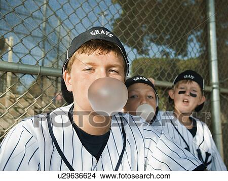 Picture - USA, California, Ladera Ranch, Boys (10-11) from little league sitting on dugout and blowing bubble gum. Fotosearch