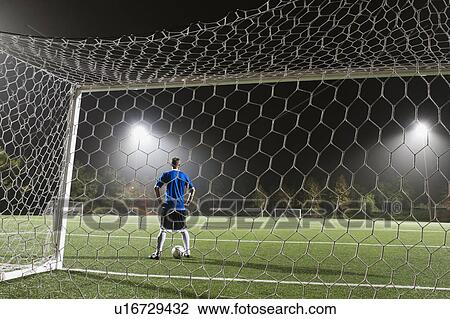 Stock Image - USA, California, Ladera Ranch, goalie on illuminated soccer field at night. Fotosearch