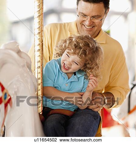 Stock Image - USA, California, Los Angeles, Father with son (4-5) sitting on carousel's horse. Fotosearch