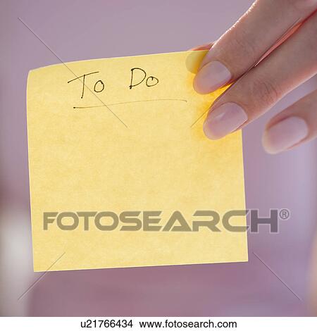 Picture - USA, New Jersey, Jersey City, Close-up view of woman hand holding adhesive note for writing down things to do. Fotosearch