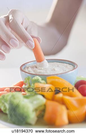 Stock Image - USA, New Jersey, Jersey City, Close-up view of woman hand putting baby carrot into dip. Fotosearch