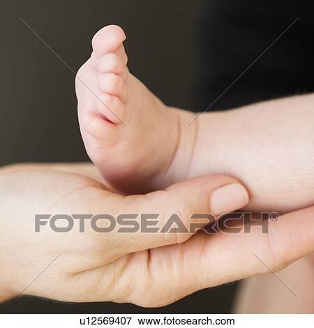 Stock Photo - USA, New Jersey, Jersey City, Close-up view of mother's hand holding baby daughter leg (2-5 months). Fotosearch