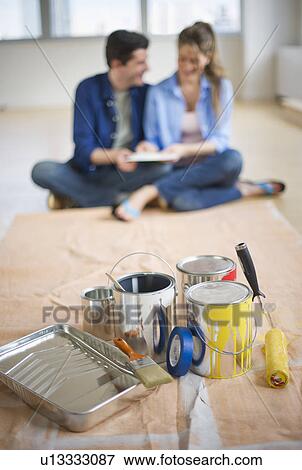 Stock Photo - USA, New Jersey, Jersey City, Couple sitting near painting equipment in new home . Fotosearch