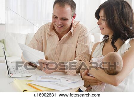 Stock Image - USA, New Jersey, Jersey City, Family with baby daughter (2-5 months) reading correspondence. Fotosearch