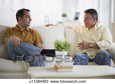 Stock Image - USA, New Jersey, Jersey City, Father and son talking on sofa in living room. Fotosearch