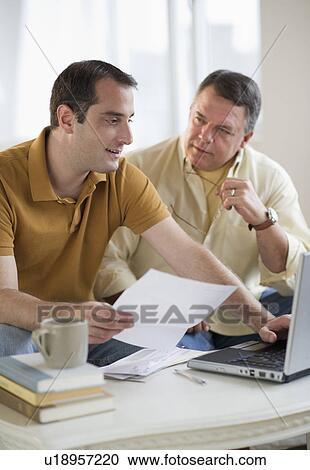 Stock Image - USA, New Jersey, Jersey City, Father and son using laptop in living room. Fotosearch