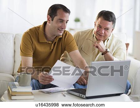 Stock Photo - USA, New Jersey, Jersey City, Father and son using laptop in living room. Fotosearch