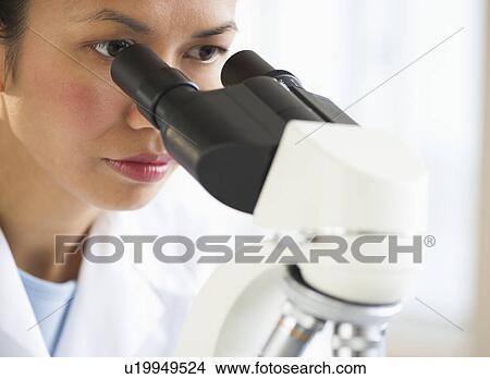 Picture - USA, New Jersey, Jersey City, Female scientist using microscope. Fotosearch