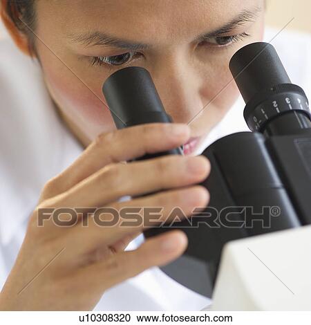 Stock Image - USA, New Jersey, Jersey City, Female scientist using microscope. Fotosearch