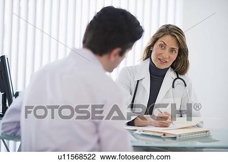 Stock Image - USA, New Jersey, Jersey City, Female doctor talking with male patient in office. Fotosearch