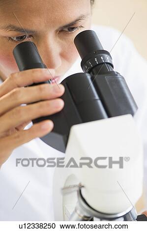 Stock Image - USA, New Jersey, Jersey City, Female scientist using microscope. Fotosearch