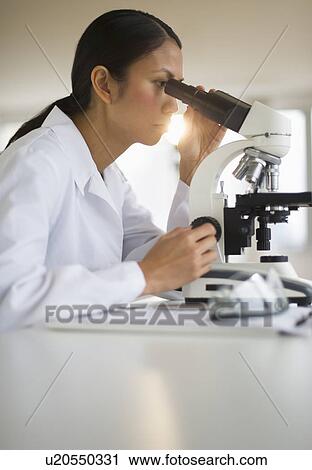 Stock Image - USA, New Jersey, Jersey City, Female scientist using microscope. Fotosearch