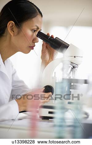 Stock Photo - USA, New Jersey, Jersey City, Female scientist using microscope behind test tubes. Fotosearch