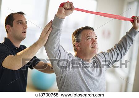 Stock Photo - USA, New Jersey, Jersey City, Fitness instructor assisting man in gym. Fotosearch