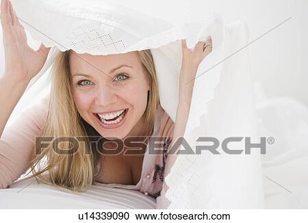 Stock Image - USA, New Jersey, Jersey City, Laughing attractive young woman emerging from under quilt. Fotosearch