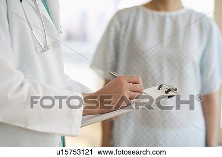 Stock Image - USA, New Jersey, Jersey City, Male doctor writing medical report with patient. Fotosearch