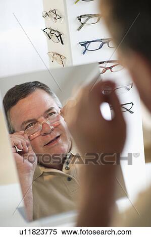 Stock Photography - USA, New Jersey, Jersey City, Man trying on glasses in shop mirror. Fotosearch