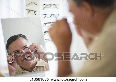 Stock Photography - USA, New Jersey, Jersey City, Man trying on glasses in shop mirror. Fotosearch