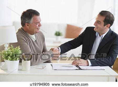 Stock Photography - USA, New Jersey, Jersey City, Man shaking hands with financial advisor in home. Fotosearch