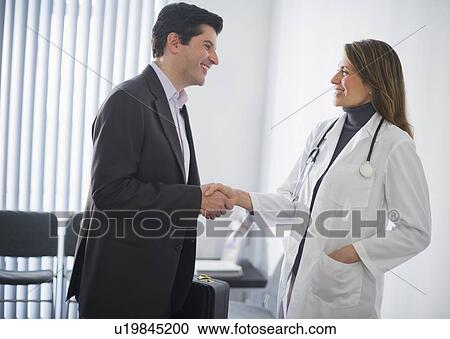 Stock Image - USA, New Jersey, Jersey City, Medical sales representative shaking hands with female doctor in office. Fotosearch
