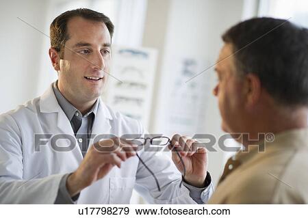 Stock Photo - USA, New Jersey, Jersey City, Optician showing man glasses in shop. Fotosearch
