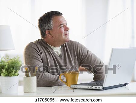 USA, New Jersey, Jersey City, Pensive man using laptop in living room View Large Photo Image Stock Image - USA, New Jersey, Jersey City, Pensive man using laptop in living room. Fotosearch