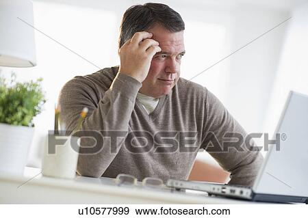 USA, New Jersey, Jersey City, Pensive man using laptop in living room View Large Photo Image Stock Photo - USA, New Jersey, Jersey City, Pensive man using laptop in living room. Fotosearch