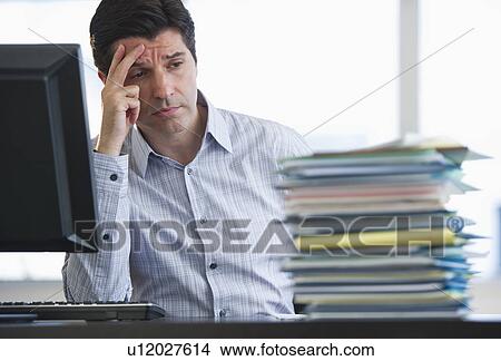 Picture - USA, New Jersey, Jersey City, Businessman staring at stacked paperwork on desk. Fotosearch