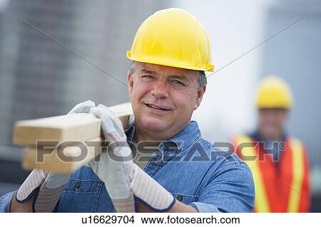 Picture - USA, New Jersey, Jersey City, Portrait of construction worker carrying planks. Fotosearch