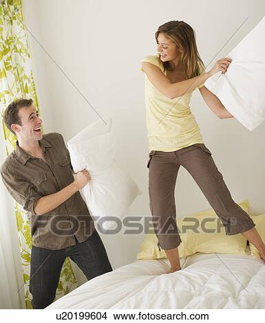 Picture - USA, New Jersey, Jersey City, Portrait of young couple fighting with pillow. Fotosearch