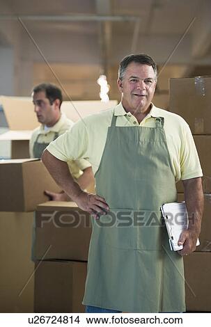 Picture - USA, New Jersey, Jersey City, Portrait of male warehouse worker by stacked boxes. Fotosearch