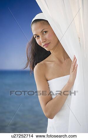 Picture - USA, New Jersey, Jersey City, Portrait of woman peering around curtain near sea. Fotosearch