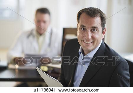 Stock Image - USA, New Jersey, Jersey City, Portrait of male patient holding medical results in office. Fotosearch
