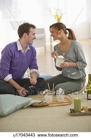 Stock Image - USA, New Jersey, Jersey City, Portrait of young couple eating takeaway food on floor. Fotosearch