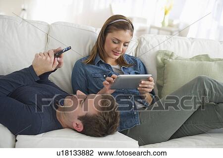 Stock Image - USA, New Jersey, Jersey City, Portrait of young couple relaxing on sofa. Fotosearch