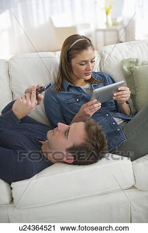 Stock Image - USA, New Jersey, Jersey City, Portrait of young couple relaxing on sofa. Fotosearch